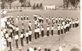 'Estudantes em apresentação no Estádio Municipal Quinzinho Nery formando o mapa do Brasil, com um rapaz segurando a bandeira nacional e garotas com fantasia alegóricas aos estados da federação 1960 a 1979