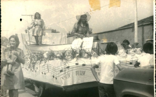 Carro alegórico com um barco e duas garotas em cima, rodeado por pessoas 1960 a 1979