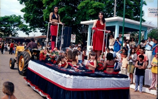 'Carro alegórico com Poliama e Fernanda e outras meniinas em desfile pela Praça Benedito Valadares, vendo-se ao fundo o coreto com o prefeito Ezequiel e outras autoridades ano 2000