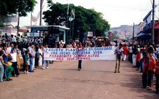 Lúcia, Maria Tereza e Deusa e outras pessoas carregando faixa do Projeto Plantando Solidariedade em desfile pela Praça Benedito Valadares ano 2000