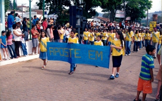 'Estudantes uniformizados em desfile cívico pela Praça Benedito Valadares, carregando faixa ano 2000