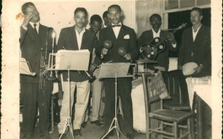 'Banda de música em momento de descontração, vendo-se Waldemar Lima vestindo terno e segurando seu trombone acompanhado por outros músicos Década de 50