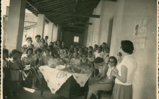 'Homenagem para as professoras da Escola Estadual Deiró Borges, sentadas a mesa Dona Alvorinda de Resende e pessoa não-identificada e em pé ao microfone a Sra. Nilda Caporali Cordeiro década de 50