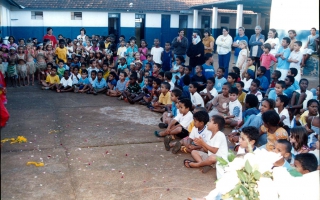 'Apresentação dos alunos da Escola Municipal Amélia Franco no pátio da escola com alunos sentados ao chão ano 2000