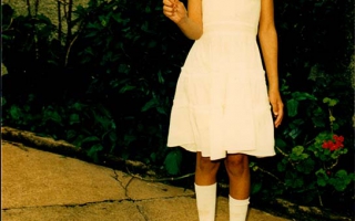 Diciene, vestida com roupas branca para a primeira eucaristia , segurando na mão direita uma vela década de 90