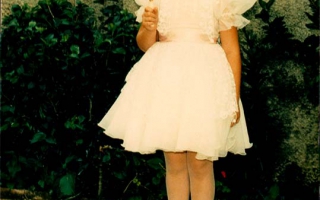 Patrícia, vestida com roupas branca para a primeira eucaristia , segurando na mão direita uma vela década de 90
