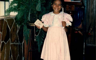 'Criança identificada como Lisamara, vestida com roupas rosa e branco  para a primeira eucaristia na Capela do Educandário Dom Alexandre, segurando nas mãos uma vela, um terço e uma bíblia década de 90