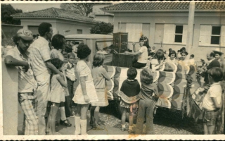 Carro alegórico sobre telefonia em desfile cívico, rodeado por pessoas e crianças, Vê-se, à direita, o fotógrafo Afonso Souza. Ano 1960-1969