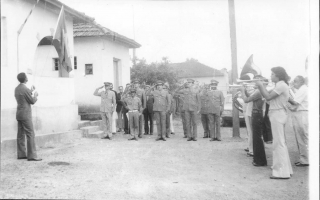 Solenidade de hasteamento da bandeira nacional, com um batalhão de policiais militares em continência e a Band Lira Santo Antônio à direita. Entre os músicos, vê-se Vicente de Paula Leandro (Paulinho), e José Bicalho.   1960-1969