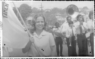 Ana Amélia Leão segurando a bandeira mineira, com a Banda Lira Santo Antônio à direita. 1970-1979