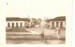'Centro da cidade de Campos Altos ao fundo o comércio Casa Alves, pessoas sentadas a praça e  mais a frente a linha férrea ano 1920