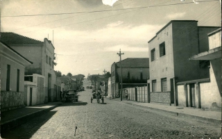 'Rua Coronel Frederico Franco na cidade de Campos Altos, ao lado direito o casarão da Sra. Inhanha em estilo colonial e o barracão da CACEC década de 40