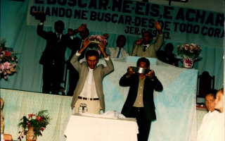 'Evangélicos em oração, no centro da foto de gravata azul Vicente ao seu lado de terno bege João do Sr. Totó, a frente do altar Vicente do Sr. Totó e ao lado direito moças não identificadas.' década de 90